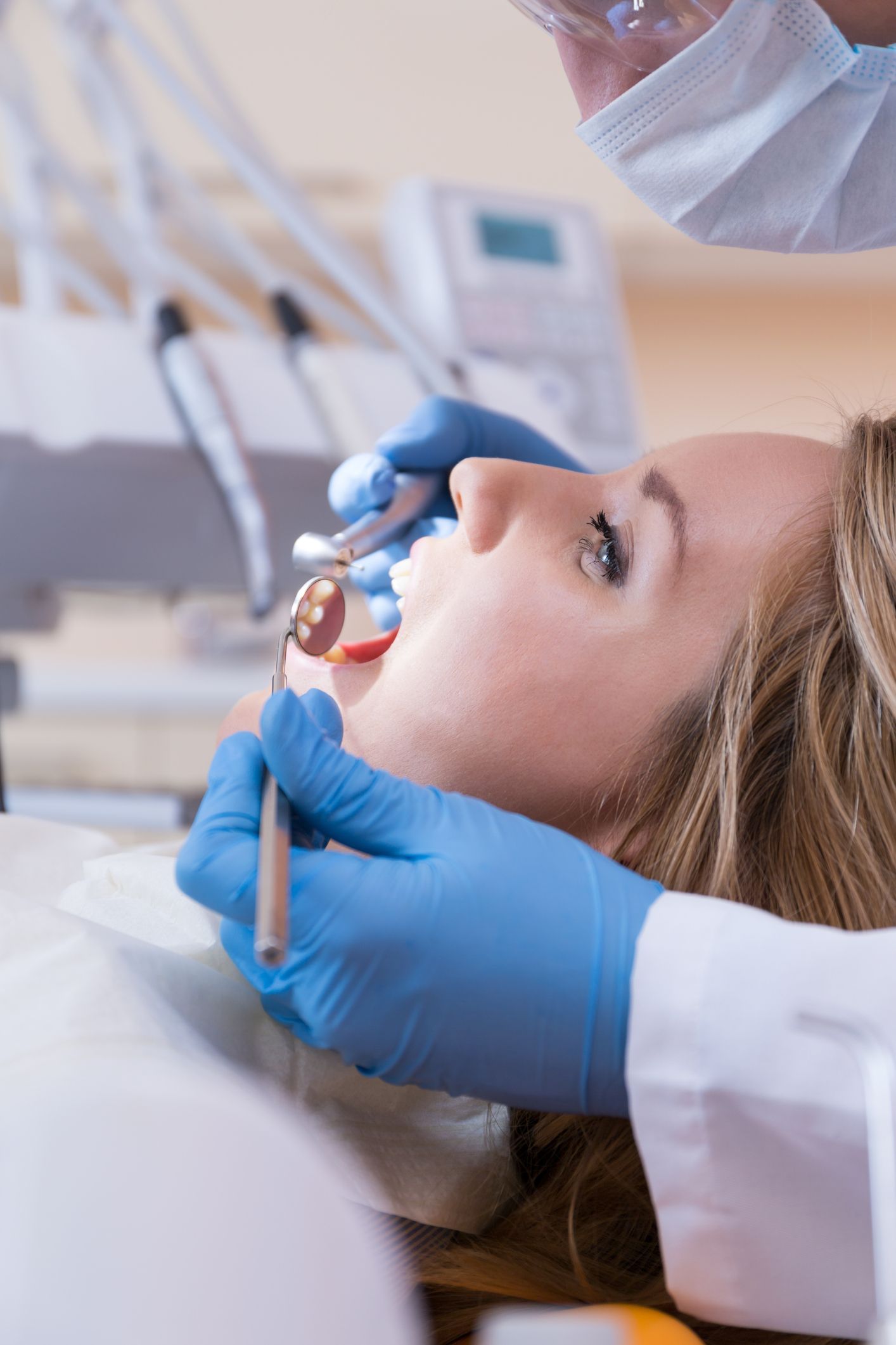 Dentist in blue gloves examining a patient’s open mouth with dental tools in a clinic