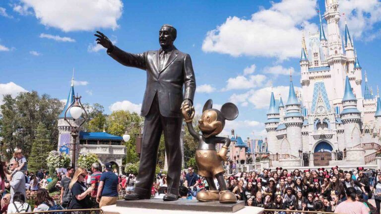 A statue of walt disney and mickey mouse in front of a crowd of people.