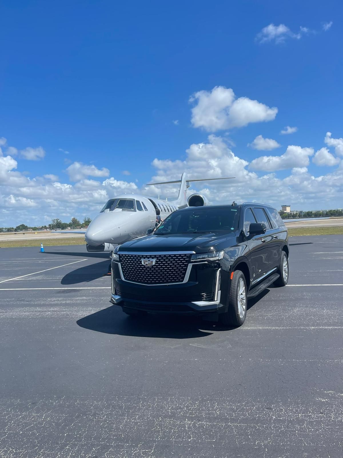 A black cadillac is parked in front of a private jet.