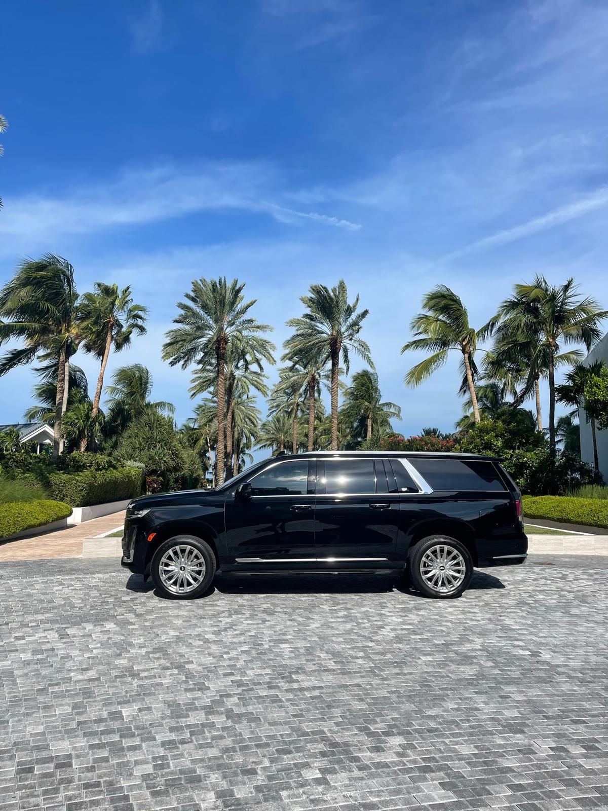 A black suv is parked on a cobblestone driveway in front of palm trees.