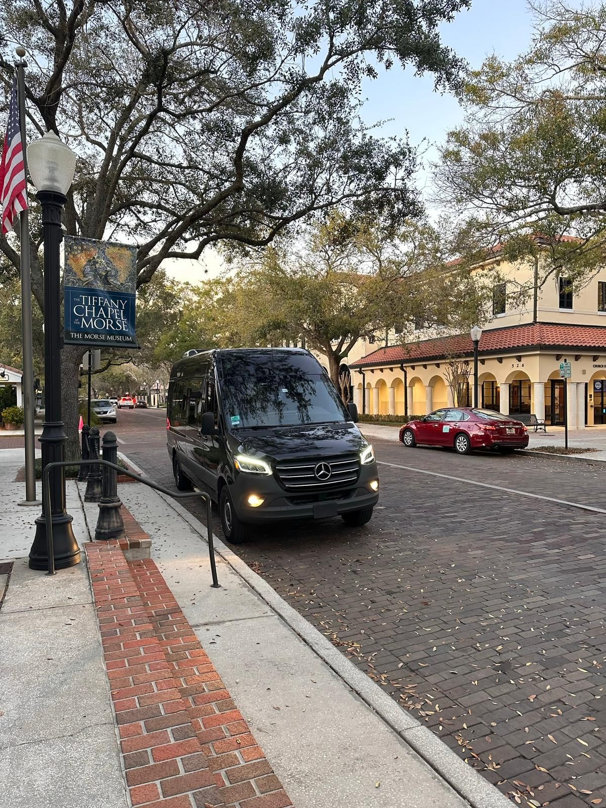 A black van is parked on the side of a brick street.
