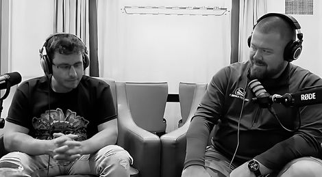Two men wearing headphones are sitting next to each other in front of a microphone.