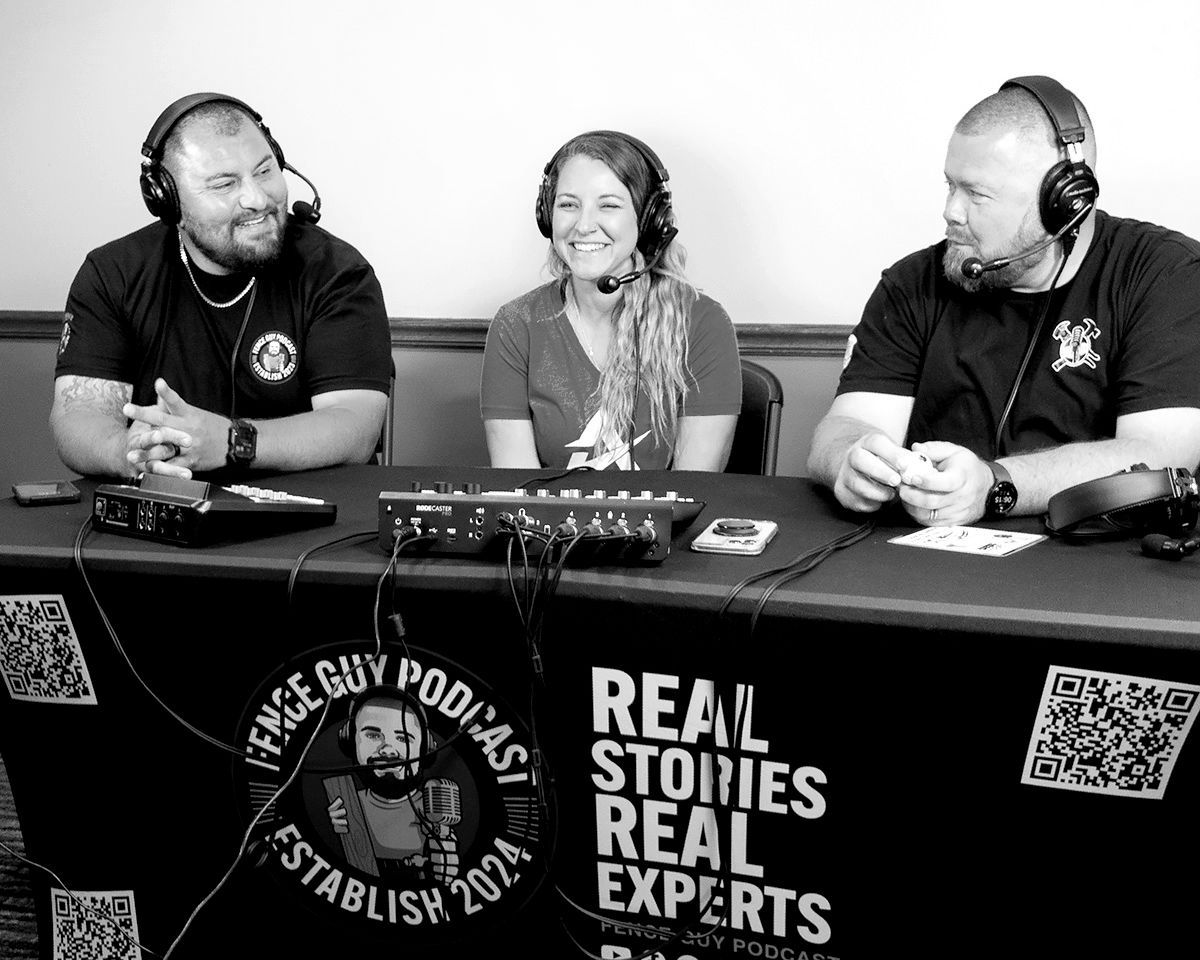Three people seated at a table, recording a podcast. A woman smiles between two men wearing headsets. The table has a logo and text.