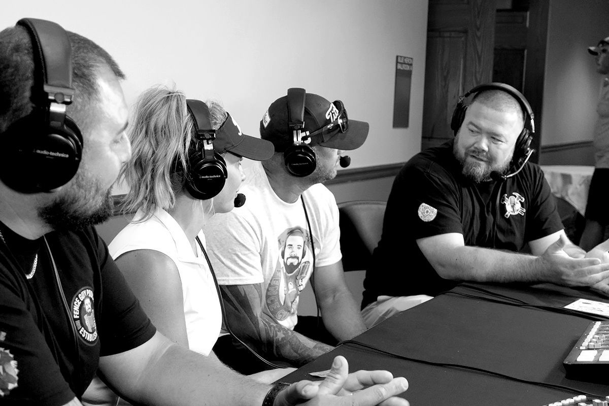 Four people wearing headsets at a table, possibly for a broadcast. They appear to be in a studio setting.
