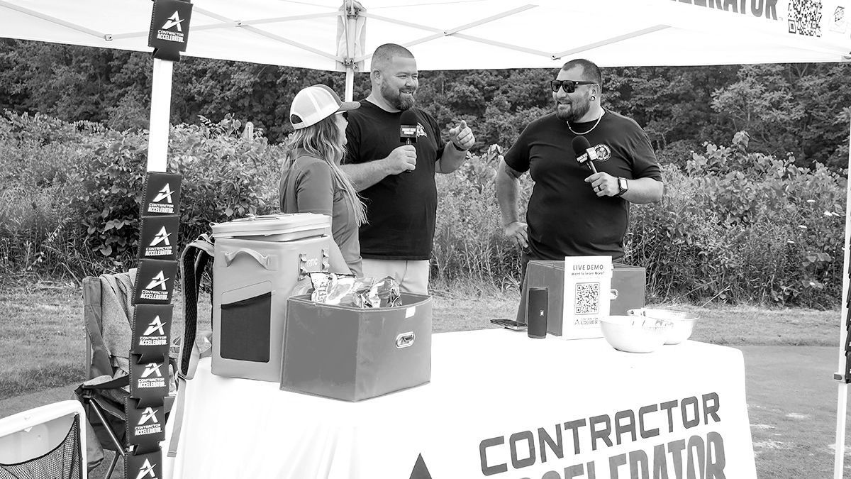 Three people at an outdoor vendor booth, one wearing a hat. 