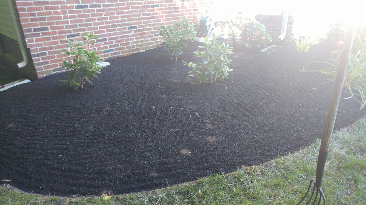 A rake is sitting in the grass next to a pile of mulch.