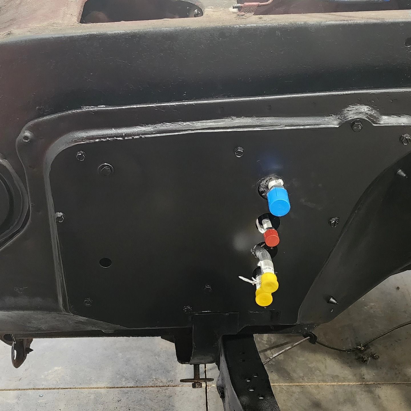 Black metal panel with blue, red, and yellow valve fittings on a machine or trailer underside