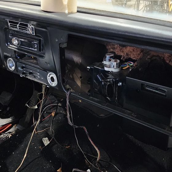 Car dashboard with the glove box removed, exposing wires and an open cavity on the passenger side.