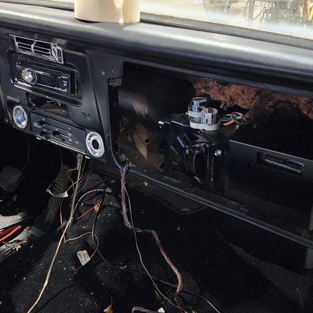 Car dashboard with the glove box removed, exposing wires and an open cavity on the passenger side.