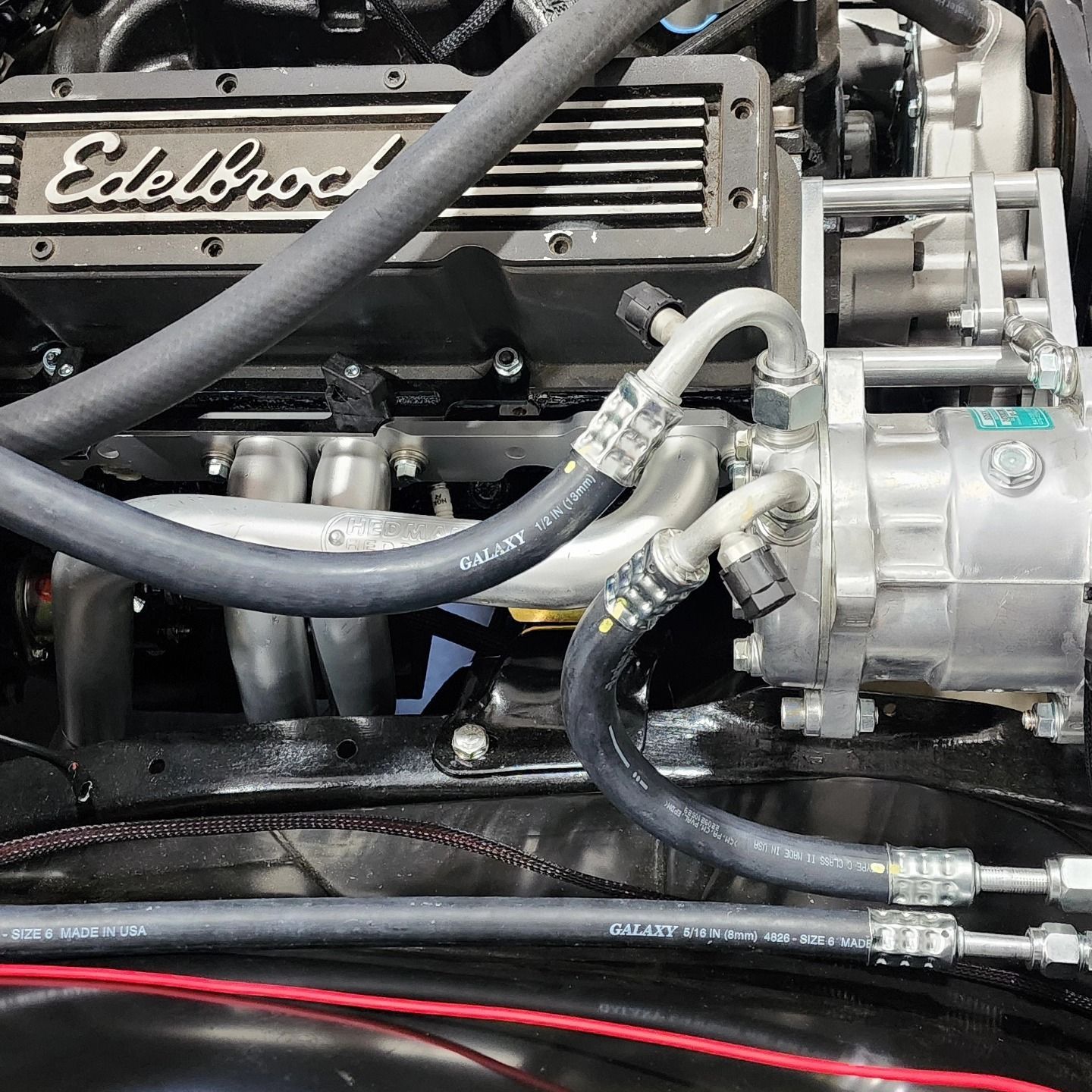 Close-up of an Edelbrock engine with hoses and a silver alternator in a car engine bay