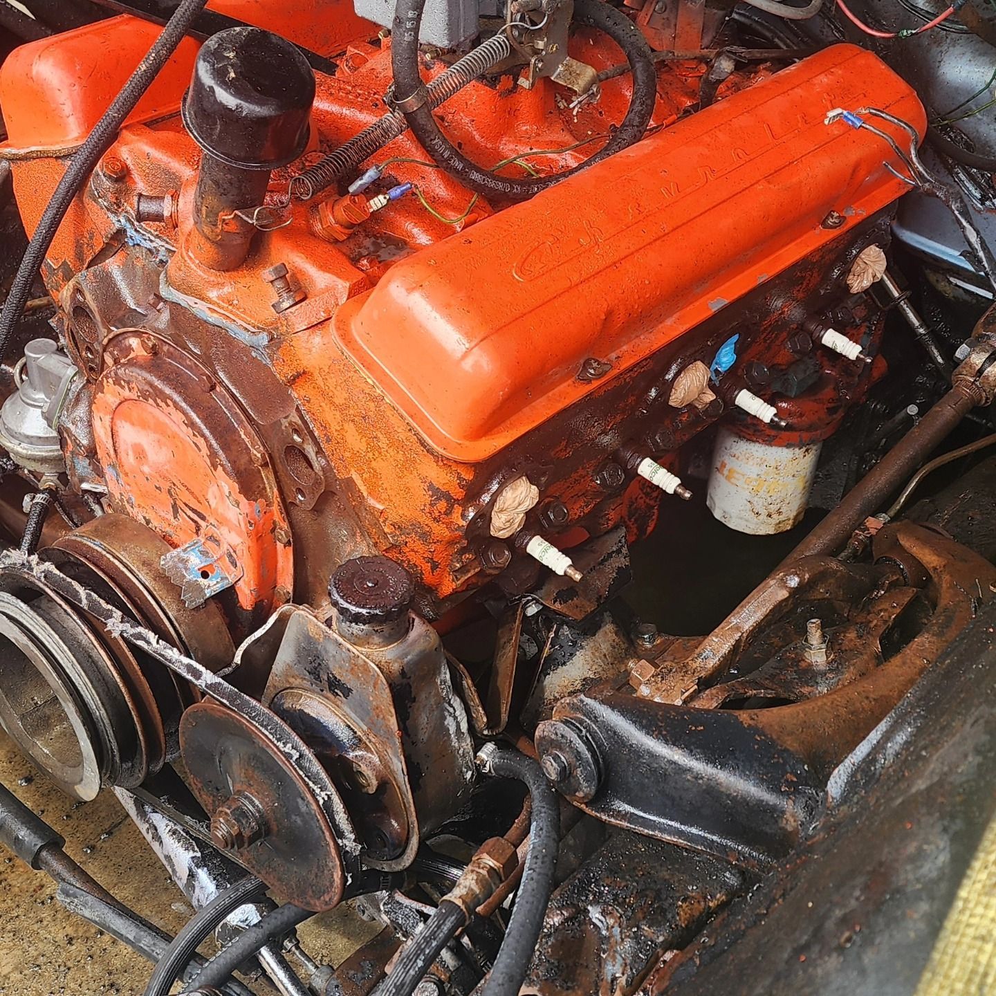 Orange car engine in a workshop, with hoses, belts, and metal components visible.