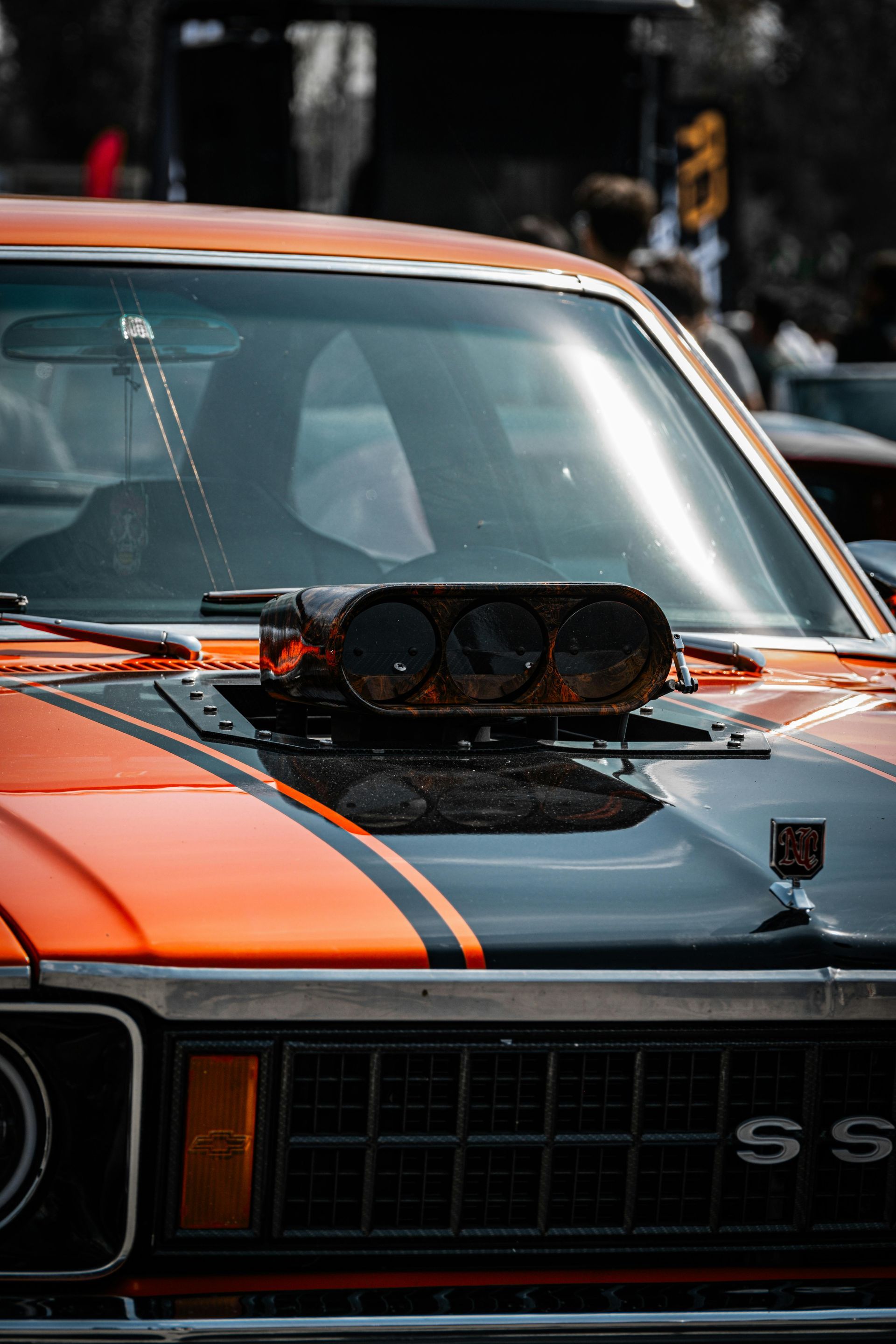 Orange classic muscle car with black racing stripes and hood scoop, front view, parked outdoors