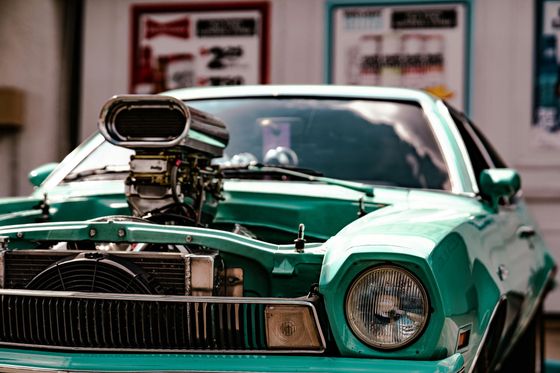 Green classic muscle car with a supercharged hood parked in front of a storefront