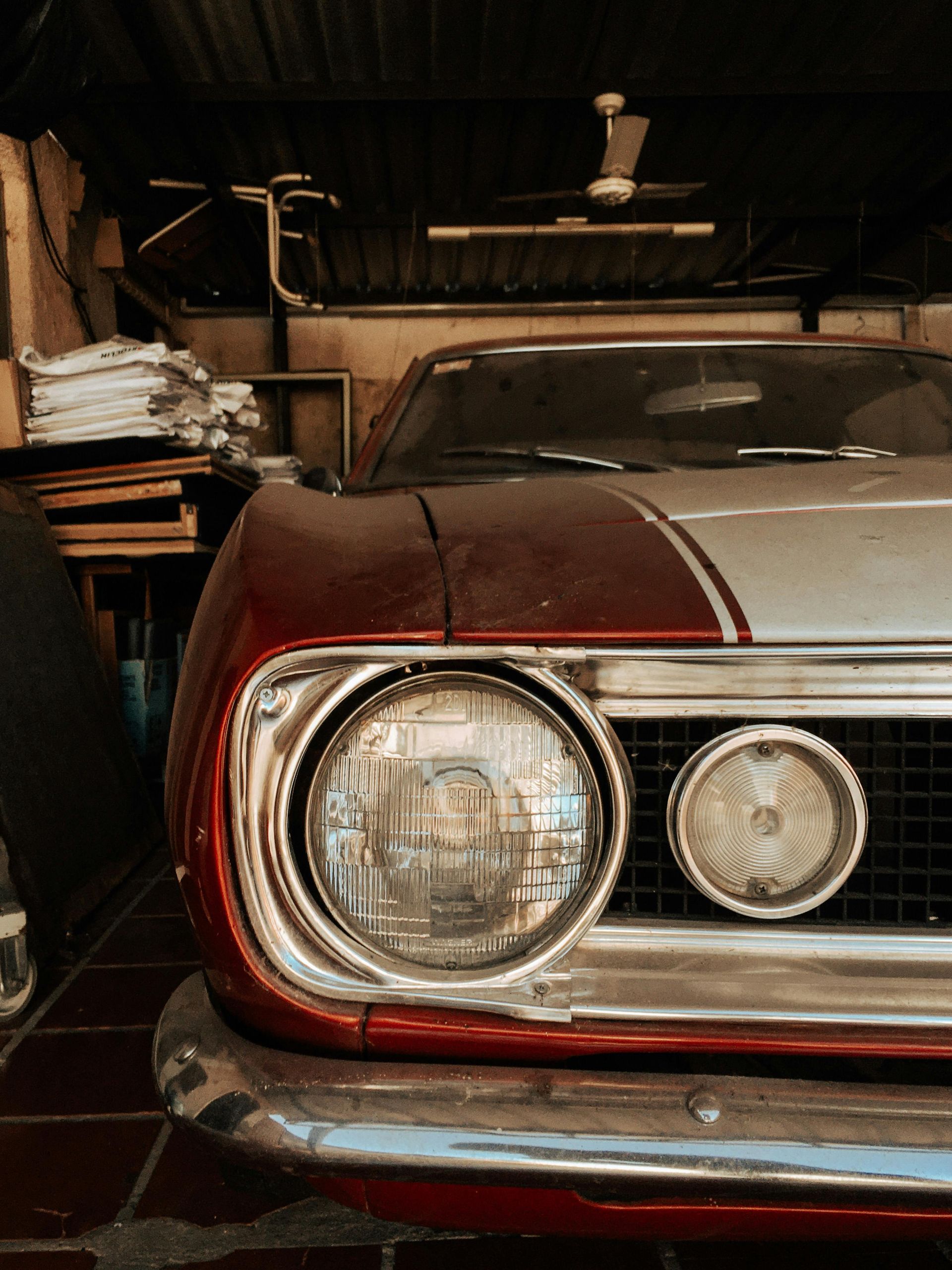 Close-up of a vintage red car parked in a dim garage with tools and shelves in the background