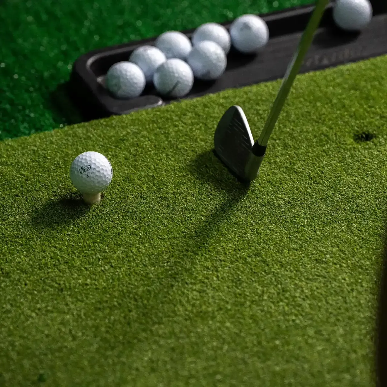 Golf ball and putter on a green practice surface near a tray of balls