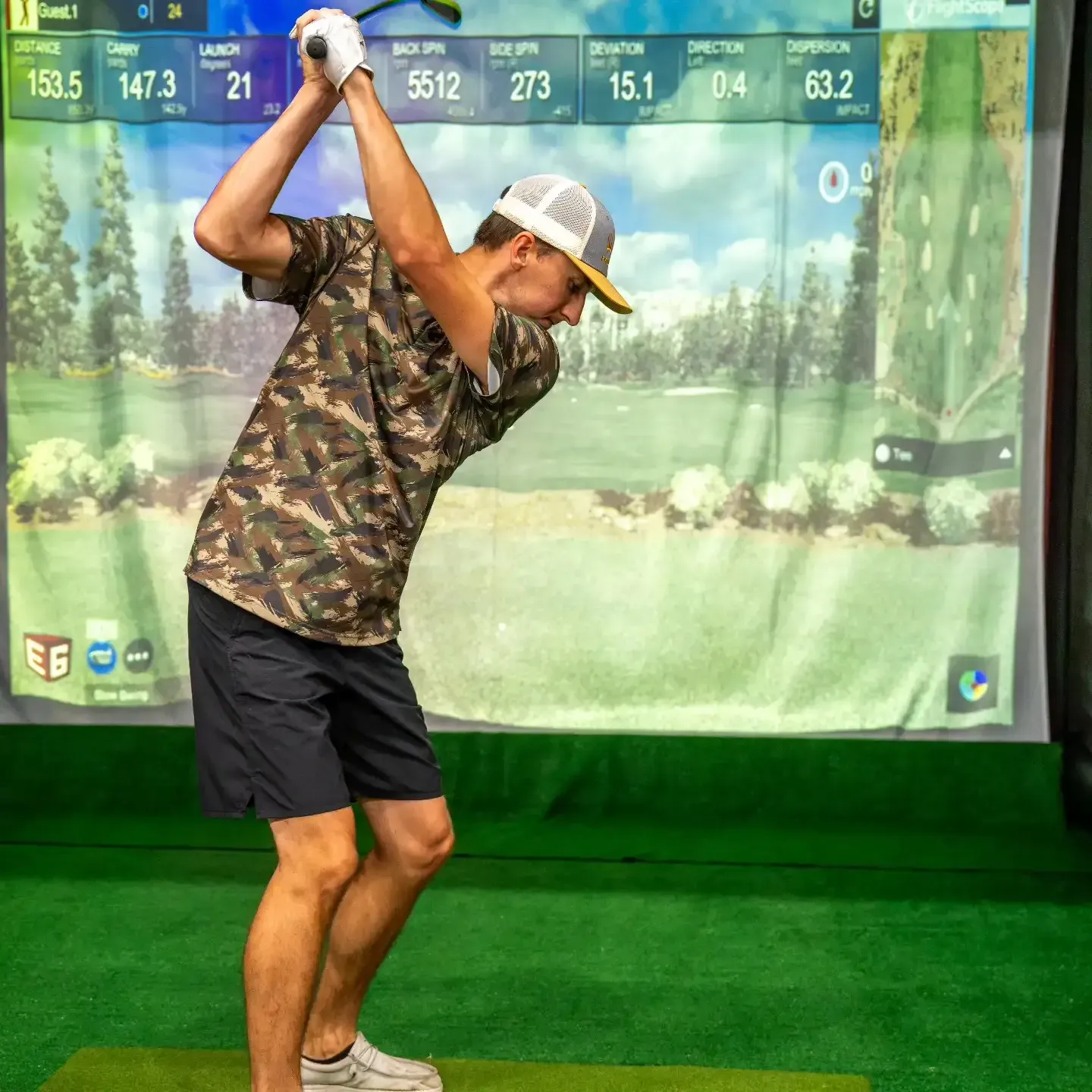 Golfer mid-swing on an indoor simulator with projected course and green turf background