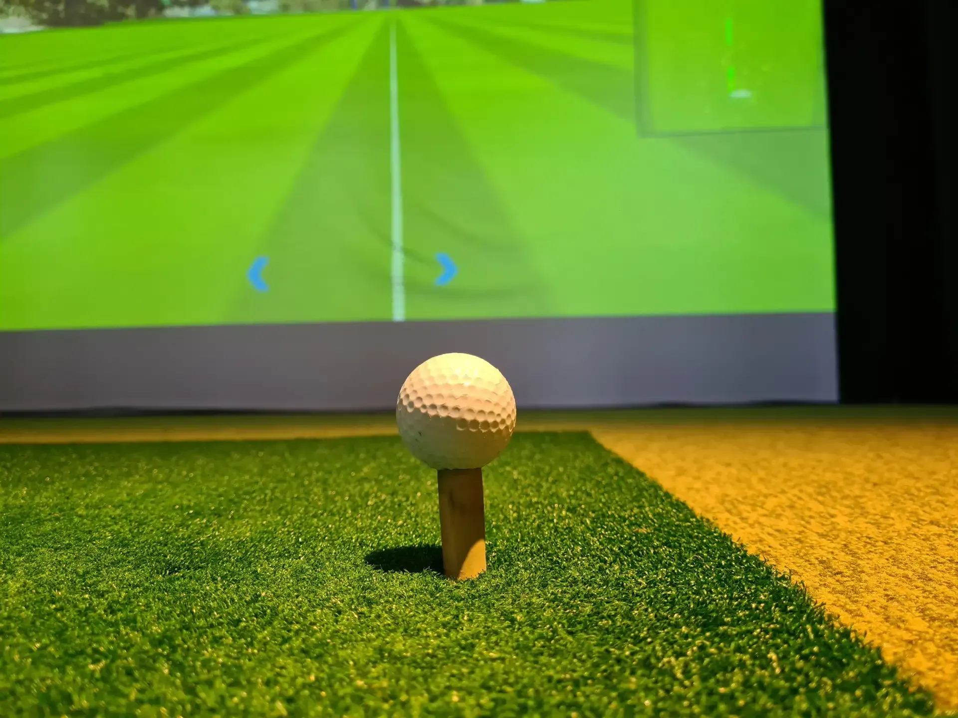 Golf ball on a tee indoors, with a virtual fairway projected behind it.
