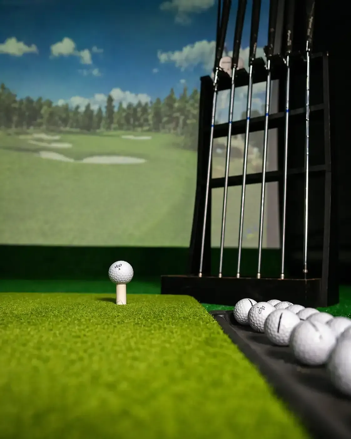 Golf ball on a tee in an indoor driving range, with clubs and practice balls beside it