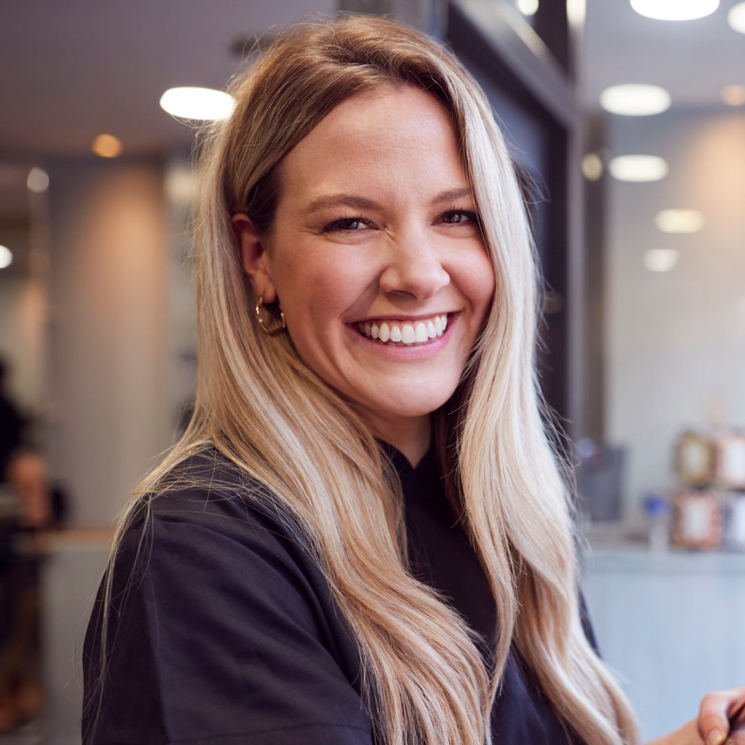 A woman with long blonde hair is smiling and wearing a black shirt.