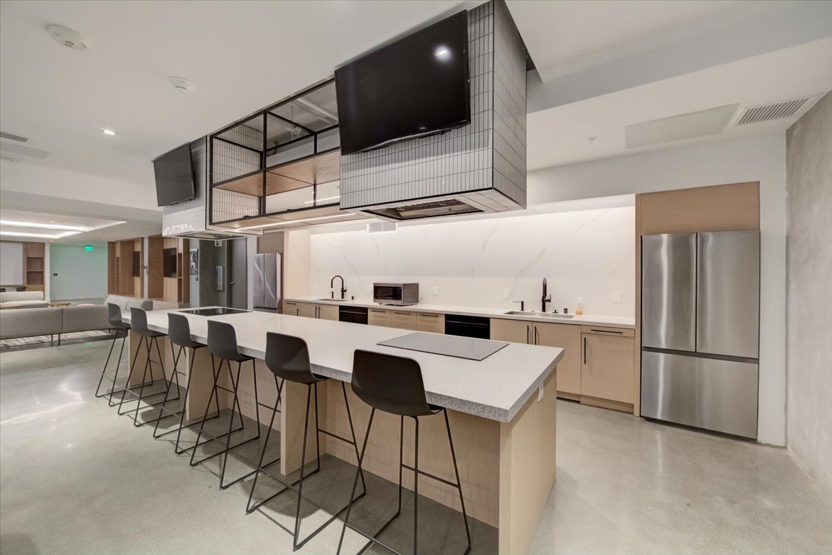 A kitchen with a large island , stools and a refrigerator.