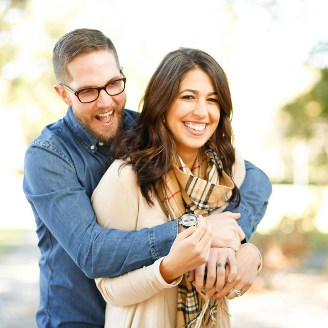 A man wearing glasses is hugging a woman wearing a scarf