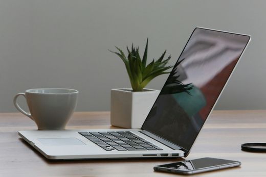 A laptop is open on a desk next to a cup of coffee and a cell phone.