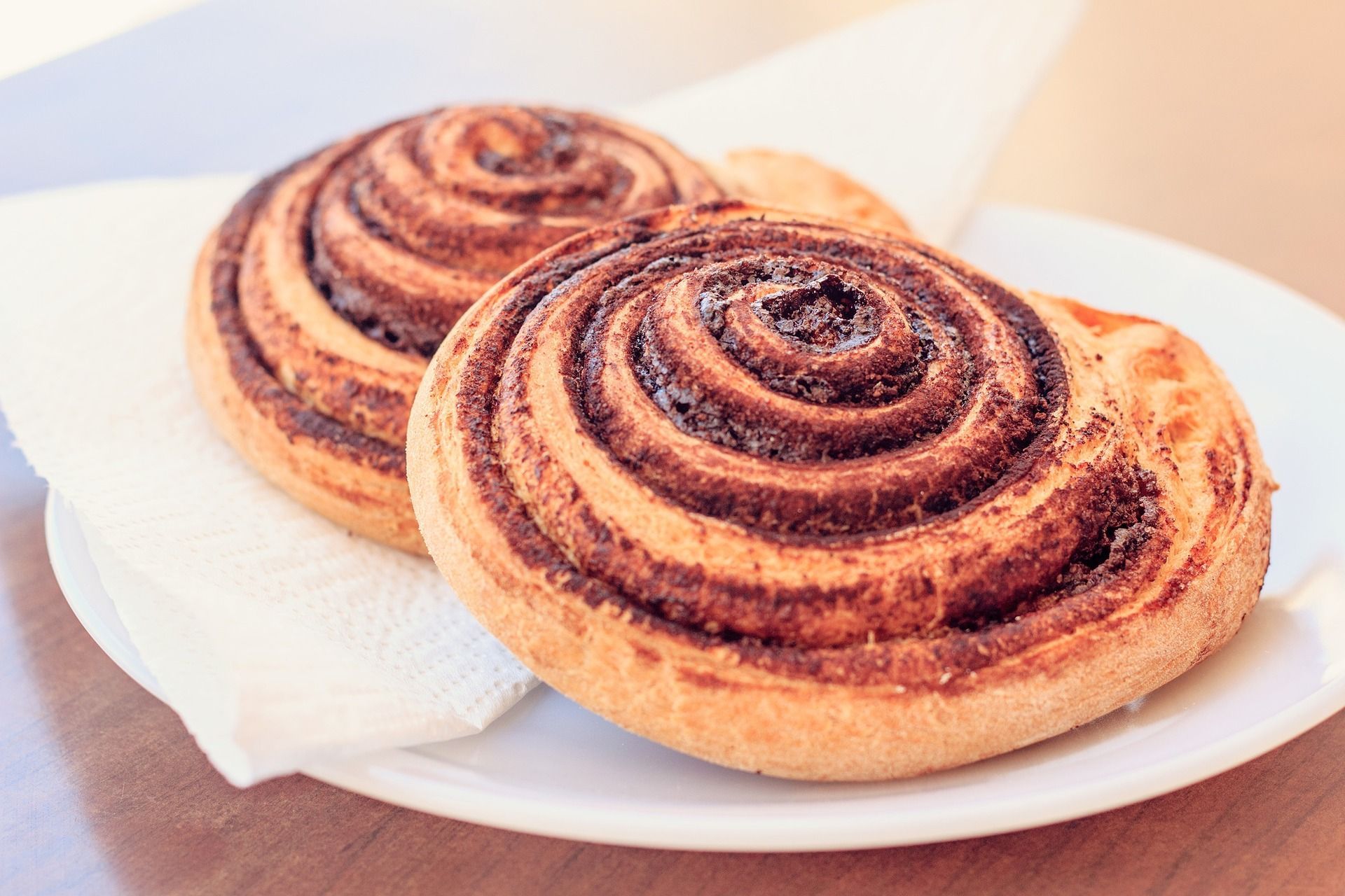 Two cinnamon rolls on a white plate with a napkin, on a wooden table.