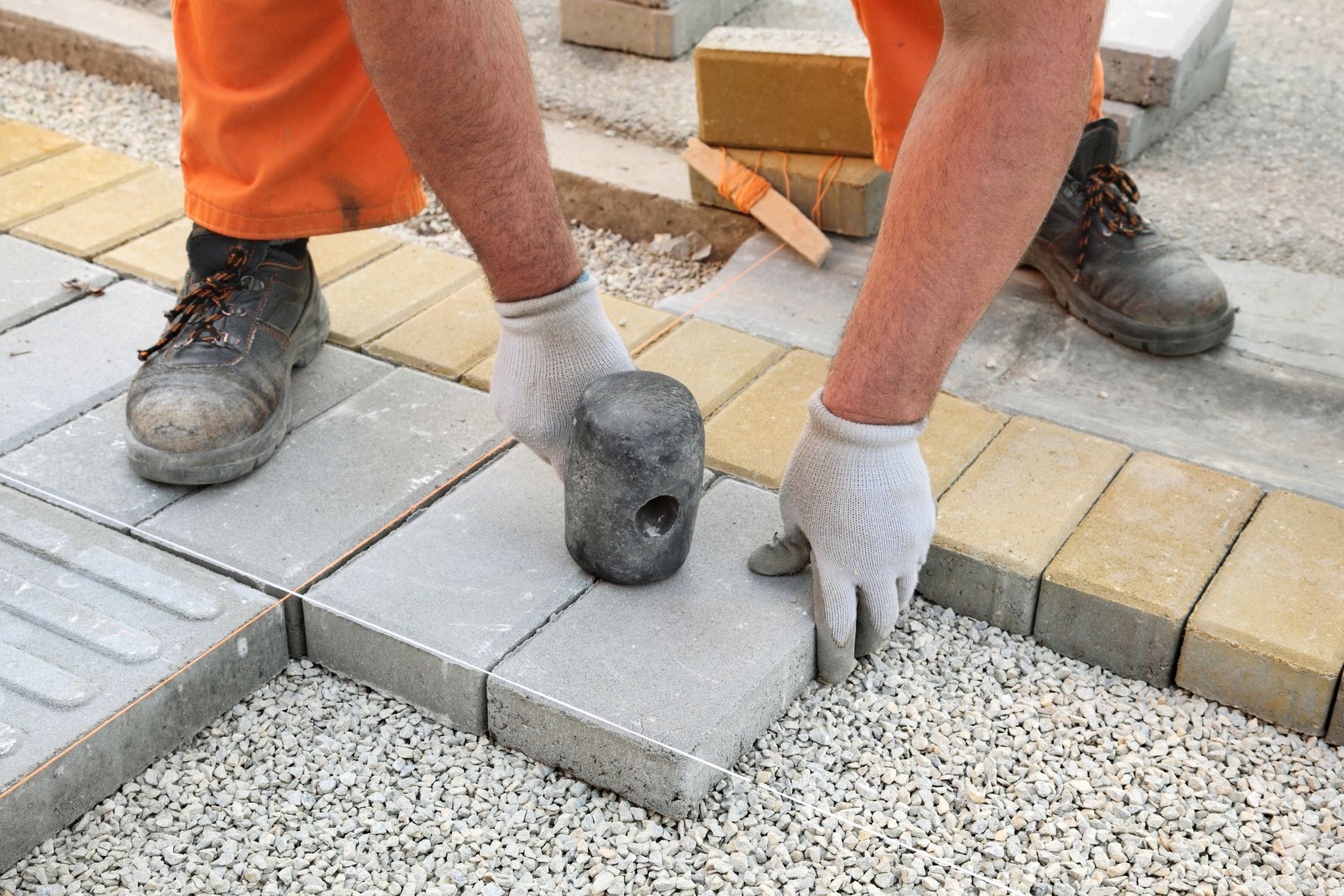 A man is laying bricks on a sidewalk with a hammer.