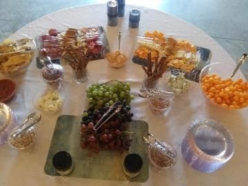 Assorted snacks and fruit arranged in bowls around a table centerpiece with wine glasses and bottles
