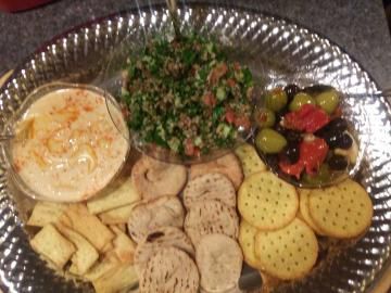 Party snack tray with dip, chopped salad, crackers, pita chips, and olives on a foil platter
