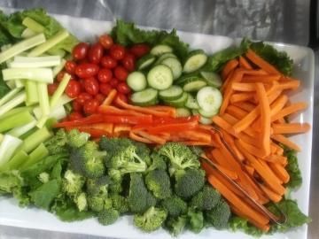 Fresh vegetables neatly arranged on a tray: broccoli, cucumbers, cherry tomatoes, celery, carrots, and red peppers.