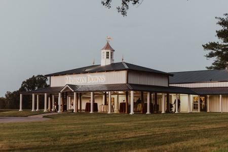 Large white barn-style building with a porch and cupola, set in a grassy field at dusk.