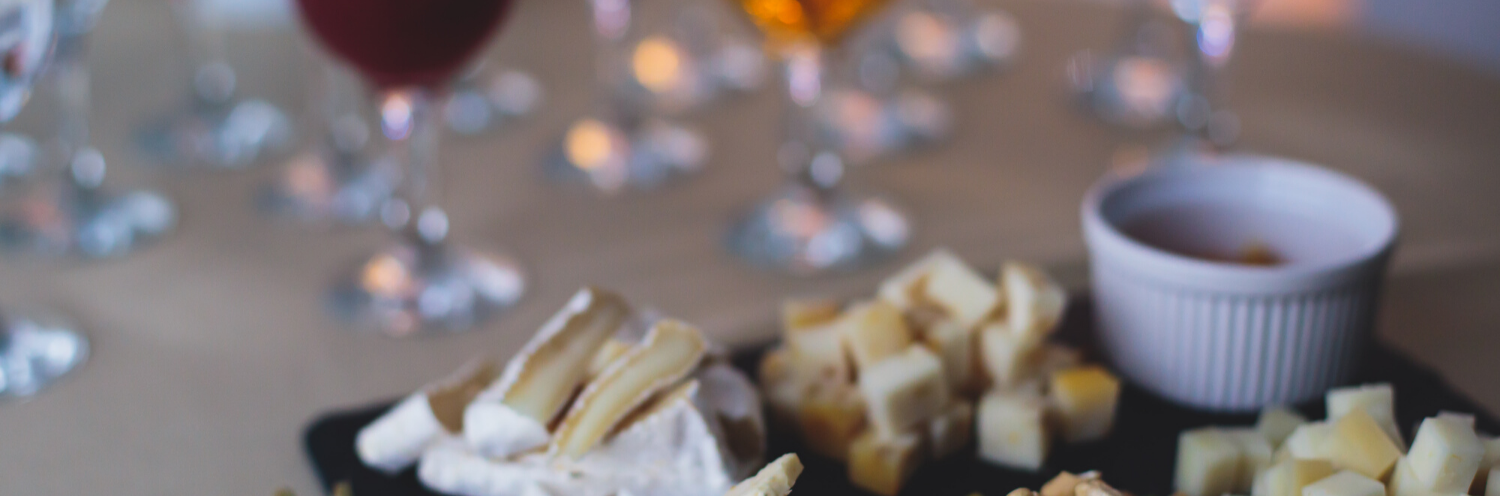 A cheese board with sliced cheese, grapes, and cups on a wooden table.