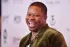 A man in a green jacket is laughing on a red carpet.