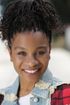 A young girl with dreadlocks is smiling for the camera while wearing a plaid shirt and a denim jacket.