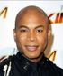 A bald man wearing a black shirt and tie smiles for the camera