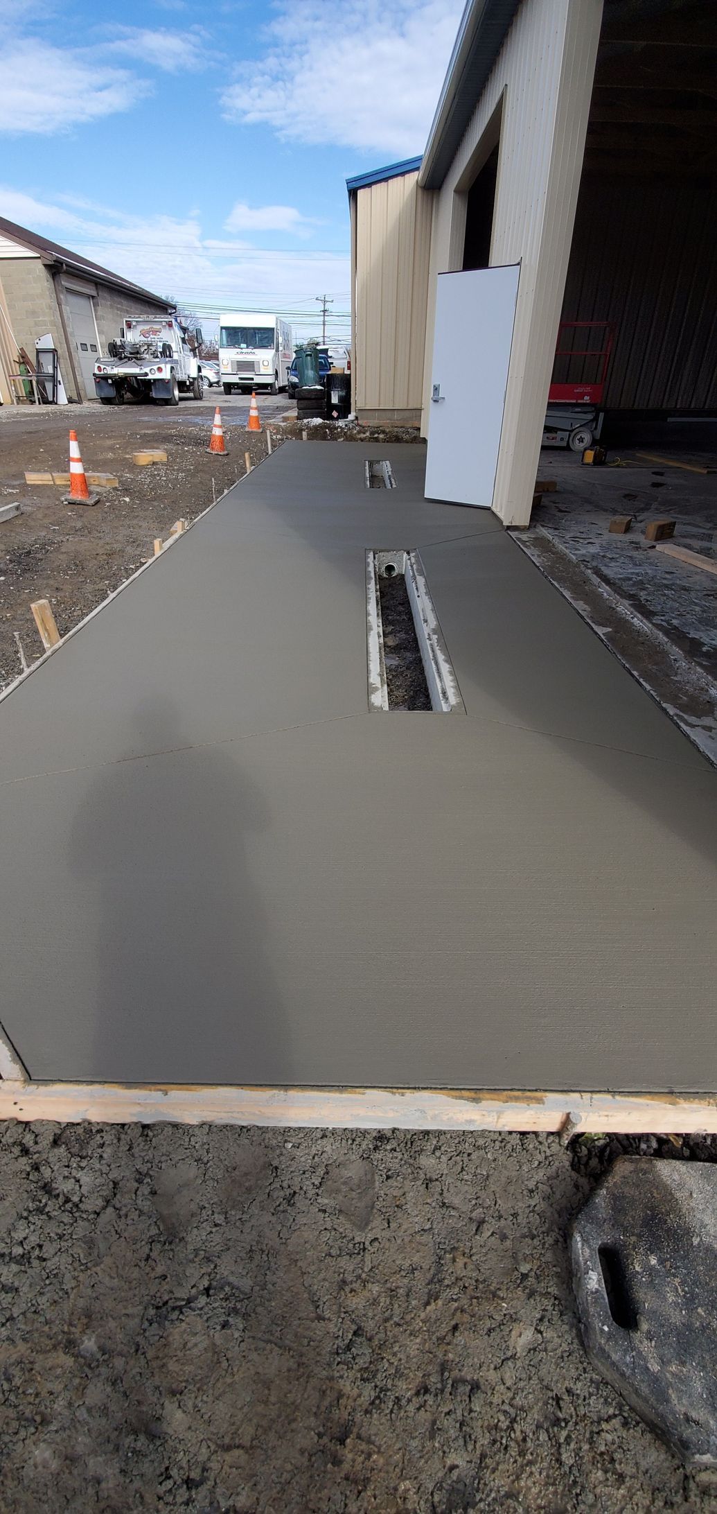 Freshly poured concrete walkway with a drain, next to a building. Construction site.