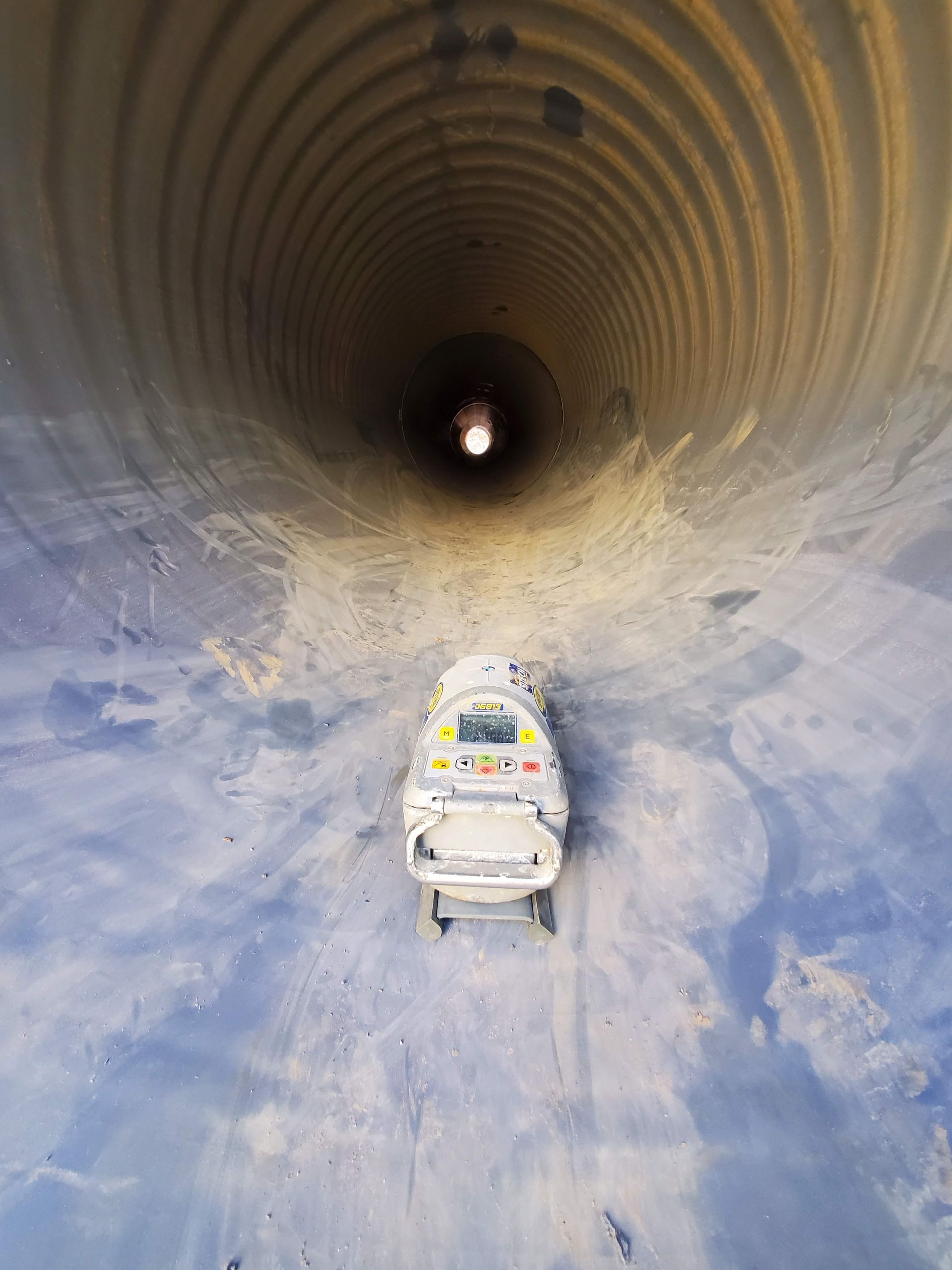A machine inside a corrugated pipe tunnel, heading toward a distant light.