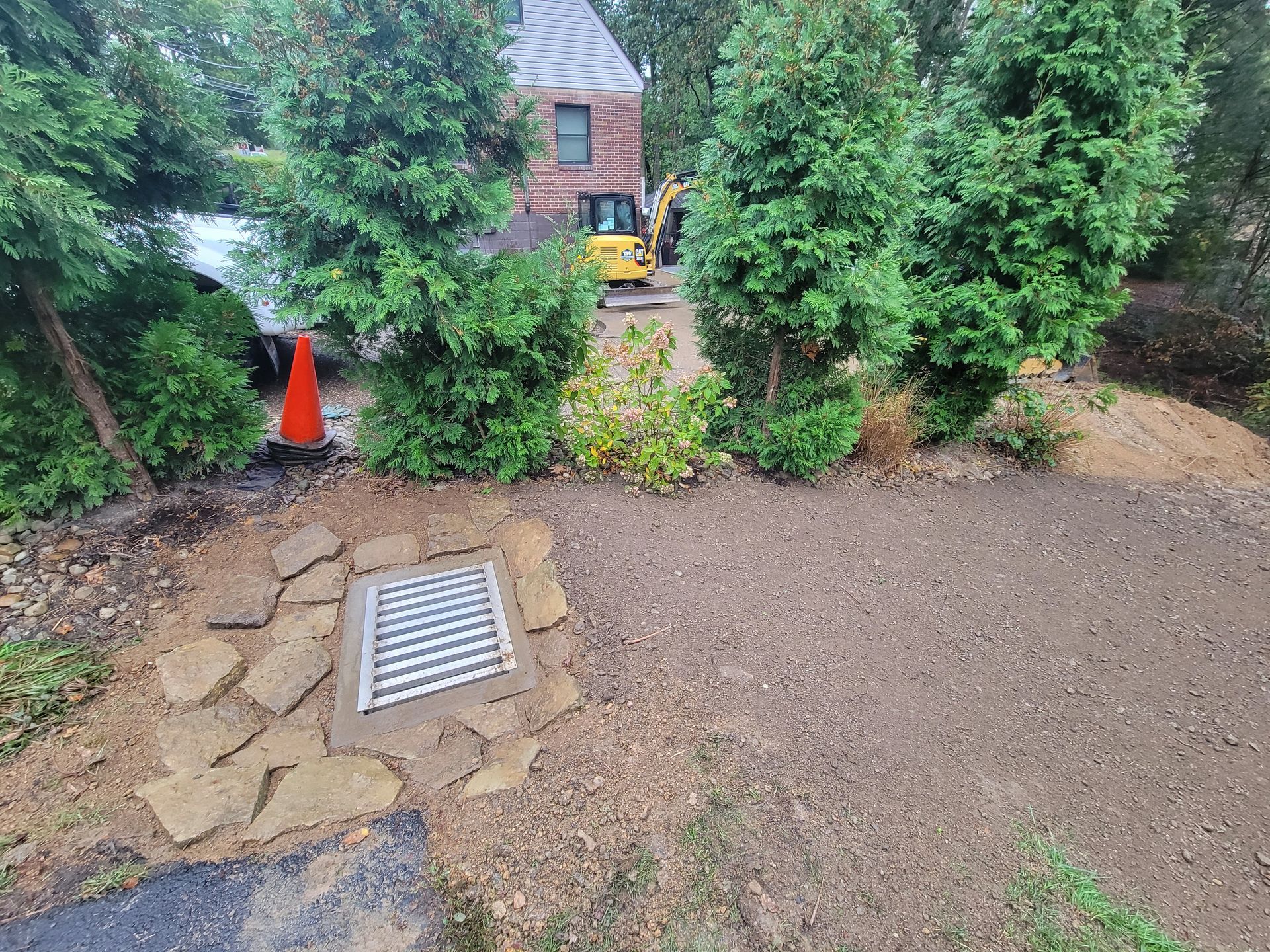 Drainage system with decorative stone, newly graded dirt, and evergreens in a residential yard.