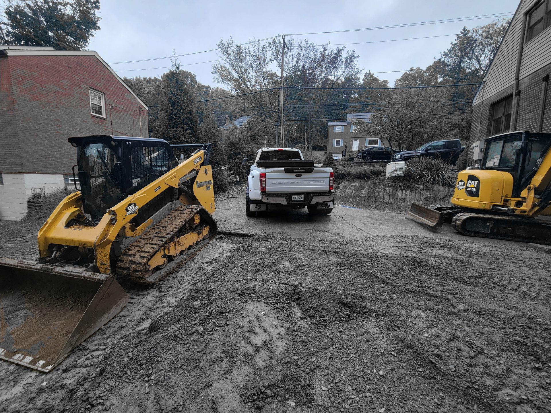 Construction site with a yellow skid steer and mini excavator, a white pickup truck, and a gray sky.