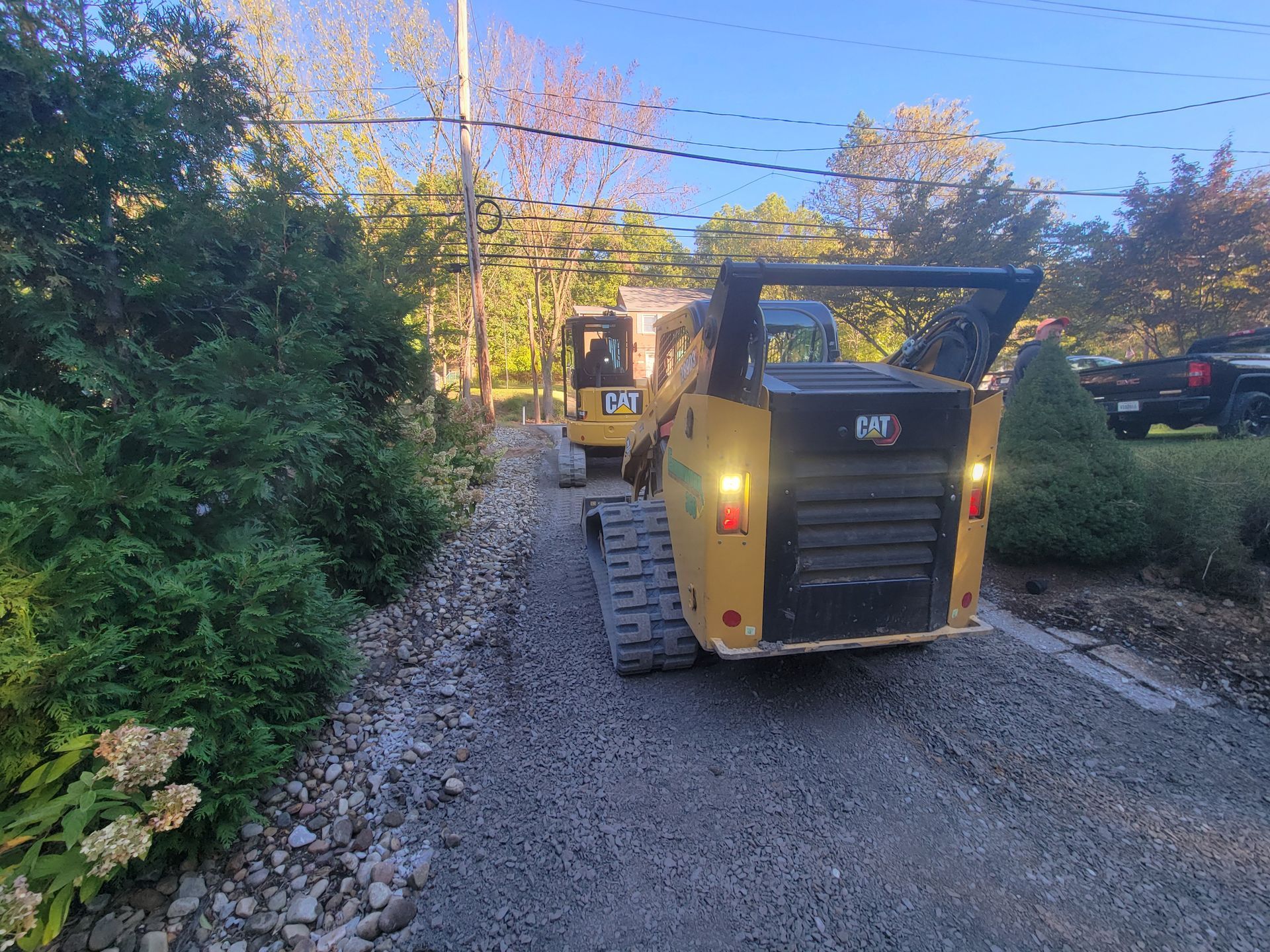 Two yellow Caterpillar skid steers on a gravel driveway, preparing a road.