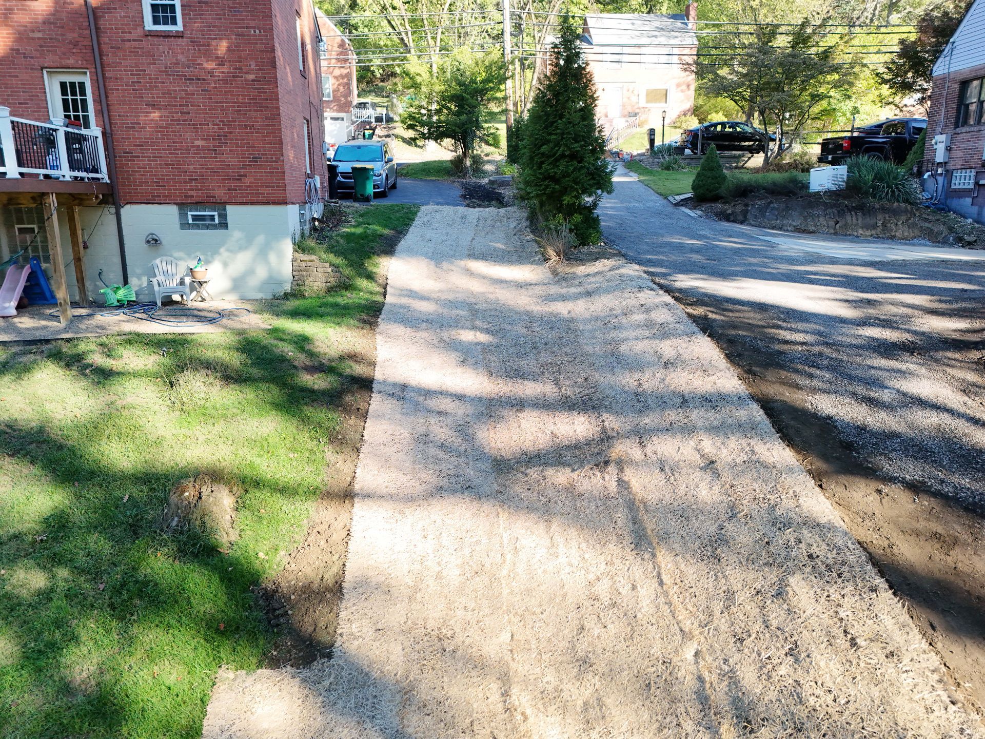 Driveway under construction with gravel, beside a green yard and brick house.