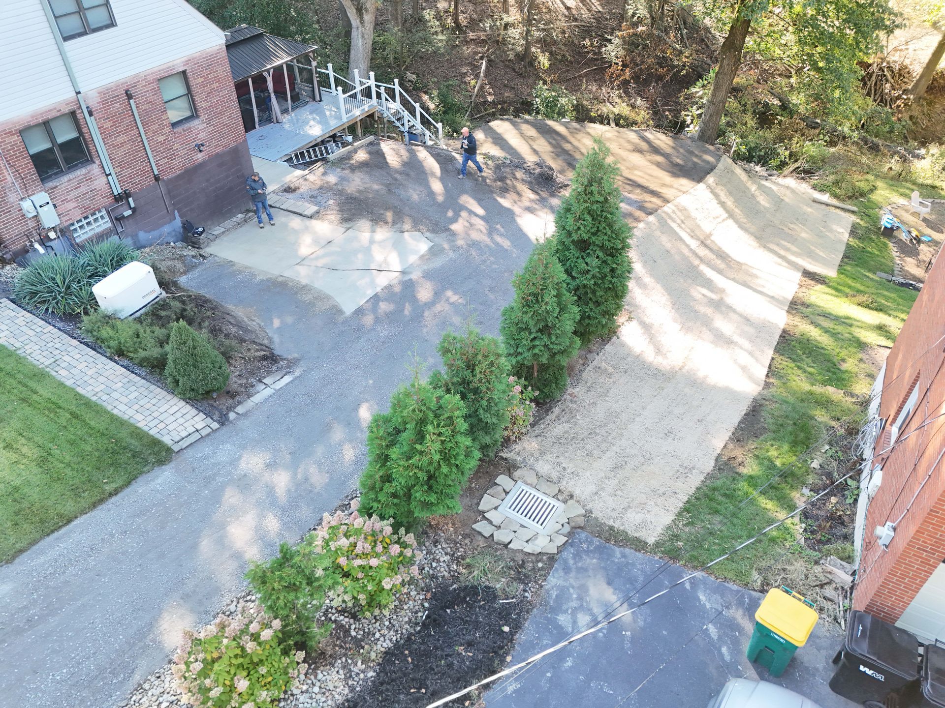 Overhead view of a house and yard with a driveway, landscaping, and two people near a deck.