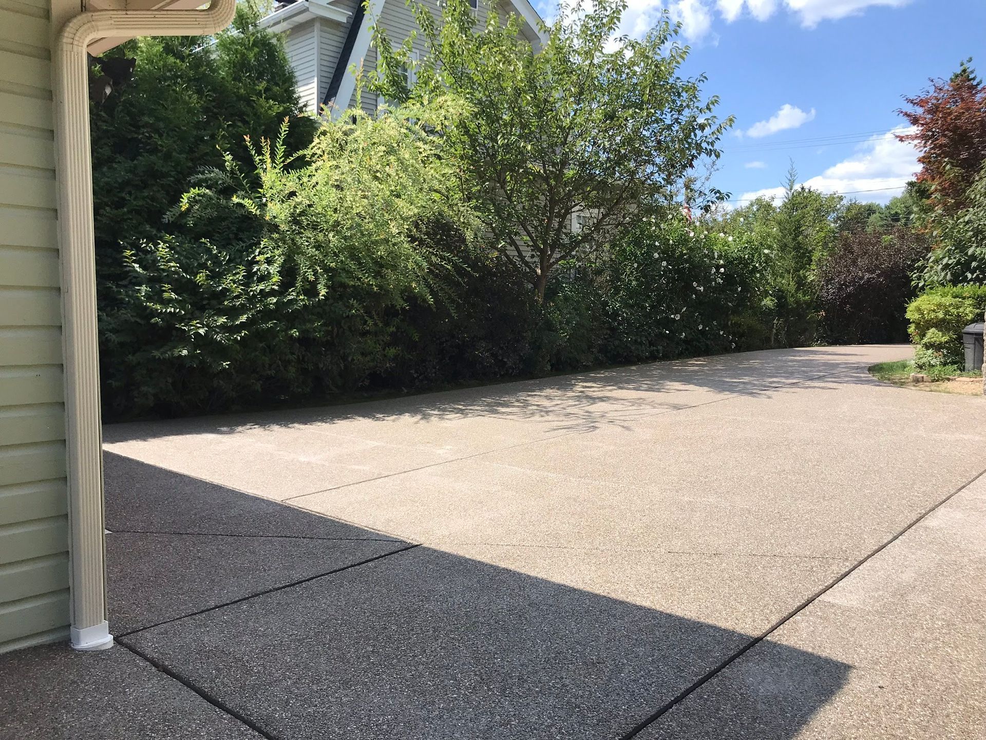 Driveway leading towards lush greenery and a partly cloudy sky.