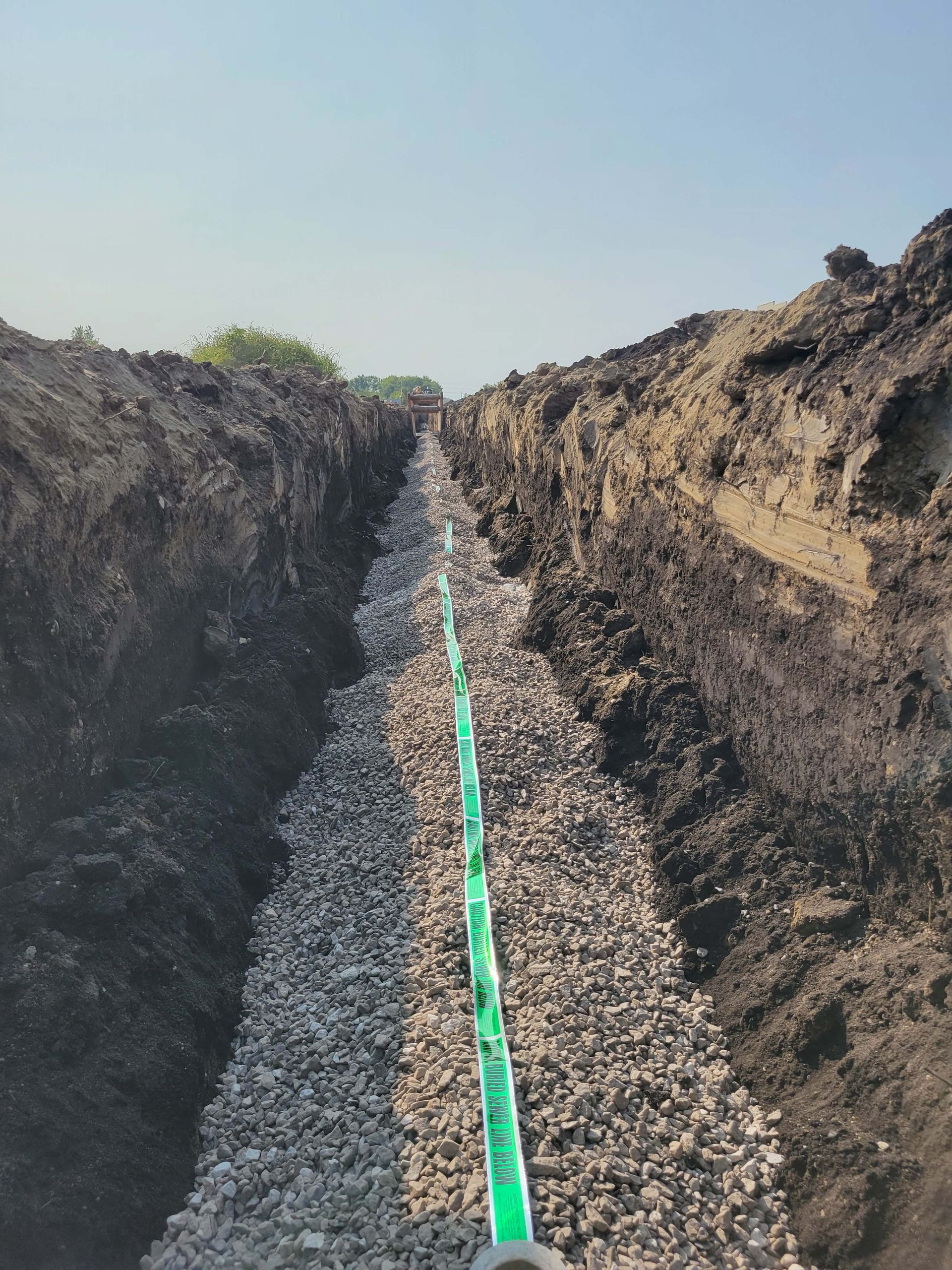 A deep trench filled with gravel, a green pipe, and a clear blue sky.