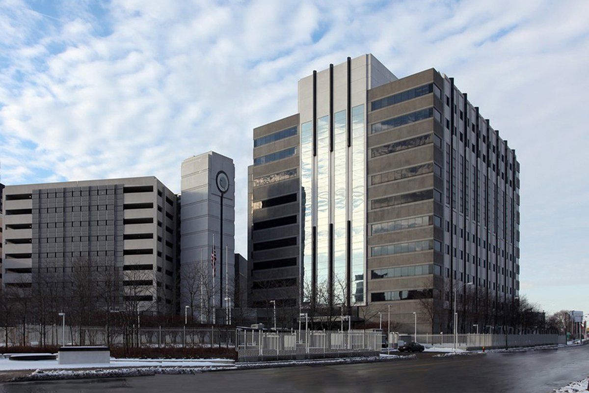 A large building with a lot of windows is surrounded by smaller buildings.