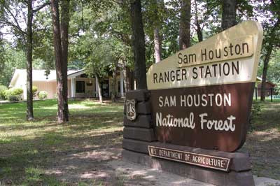 A sign for the sam houston ranger station is surrounded by trees.