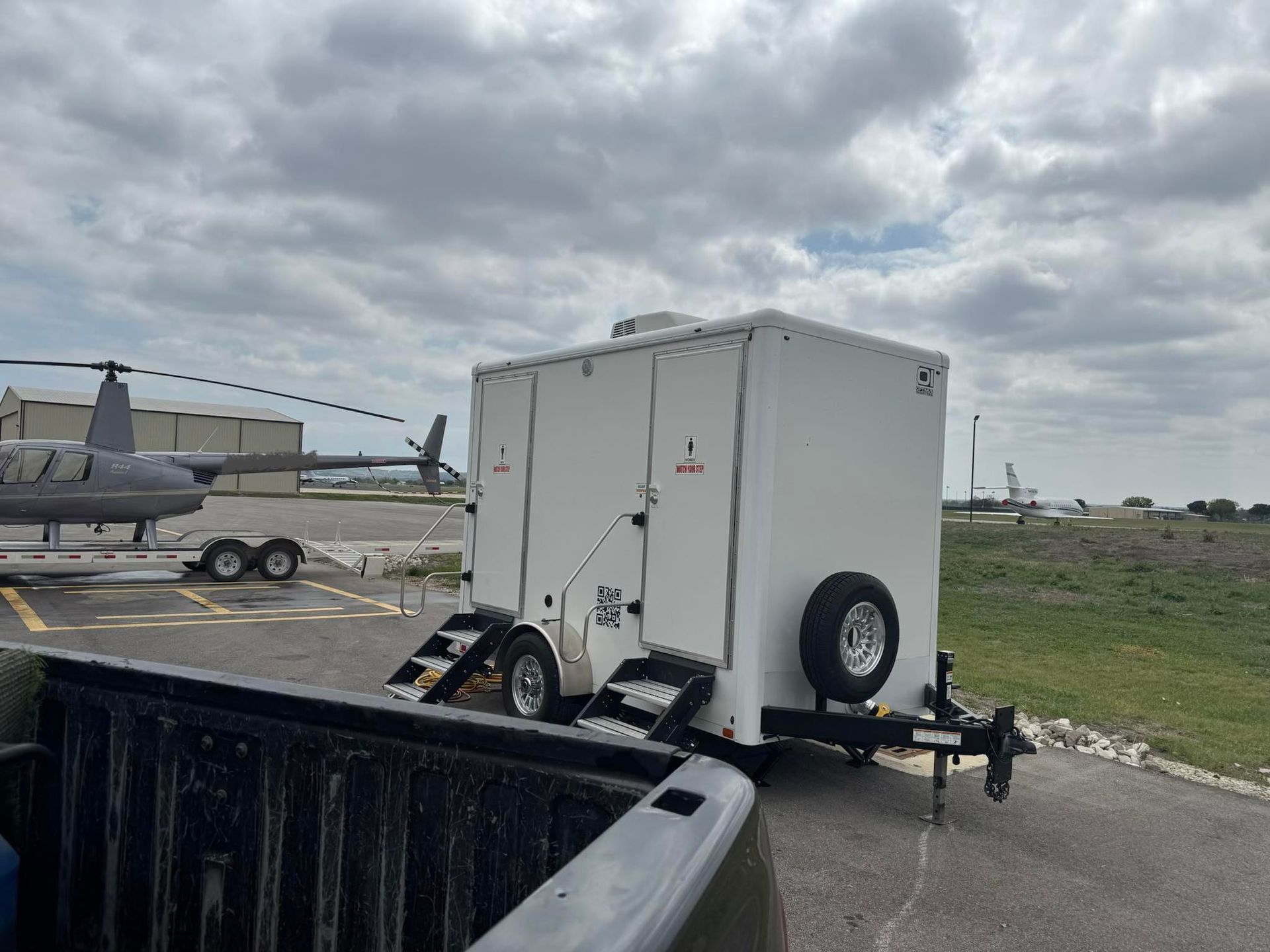 White utility trailer parked near a helicopter on a runway under cloudy skies.