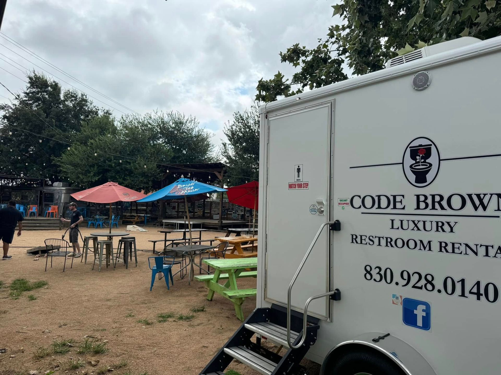 Food truck labeled “Code Brown” at an outdoor event with picnic tables and colorful tents.