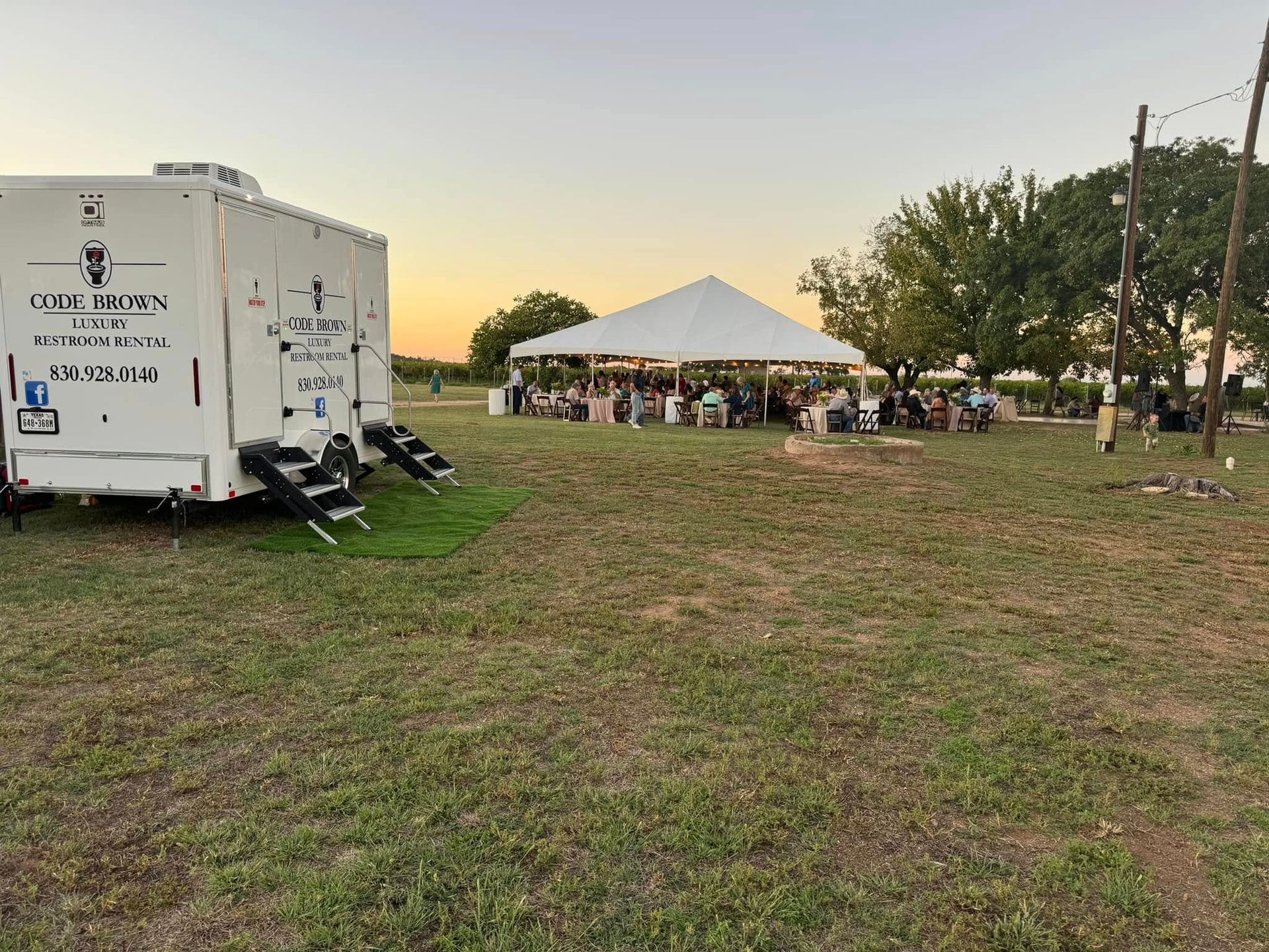 White event trailer near a tented gathering at sunset on a grassy field